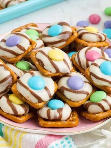 Pretzel squares topped with melted chocolate candies and pastel candy-coated chocolates arranged like flowers.