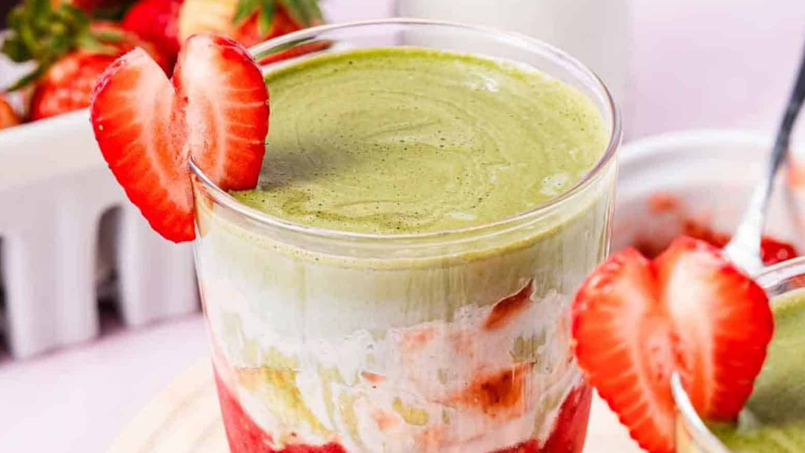 A layered strawberry and matcha dessert in a glass, garnished with a sliced strawberry on the rim.