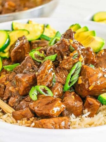 Bite-sized pieces of glazed teriyaki steak garnished with sliced green onions in a bowl over rice.