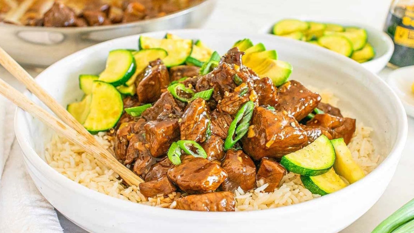 Bite-sized pieces of glazed teriyaki steak garnished with sliced green onions in a bowl over rice.
