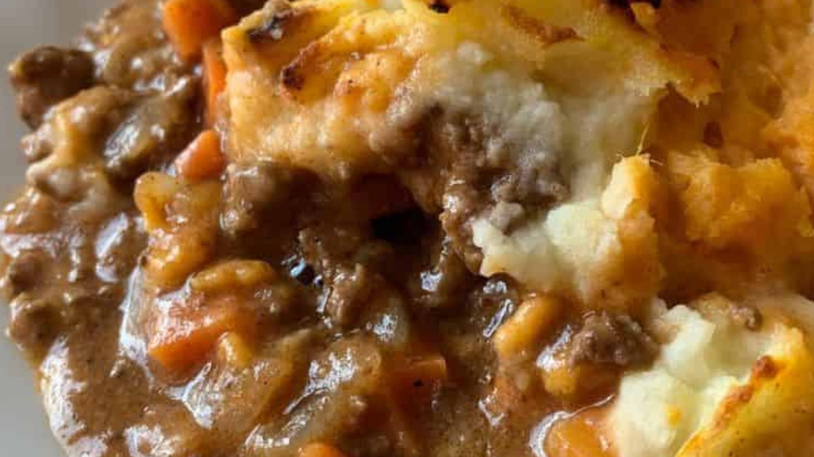 A plate with cottage pie casserole and a side of mixed greens on a white surface, accompanied by an orange-patterned cloth in the background.
