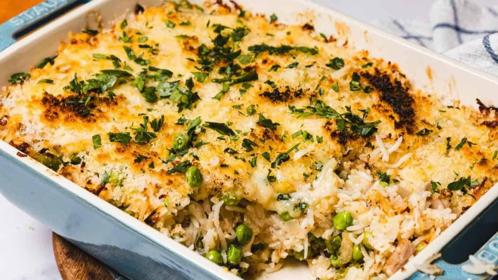 A baked casserole topped with melted cheese and herbs, with rice and green peas visible inside.