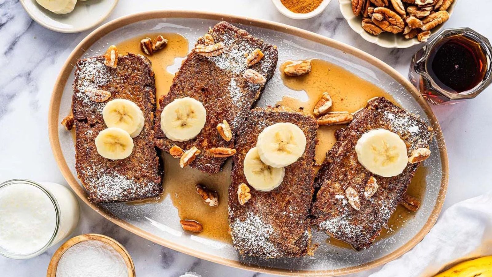 Slices of banana bread French toast topped with banana slices and syrup on a plate.