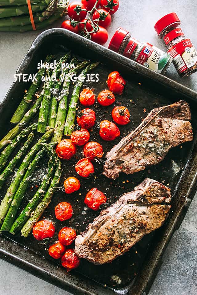cooked steak with tomatoes and asparagus on baking sheet.