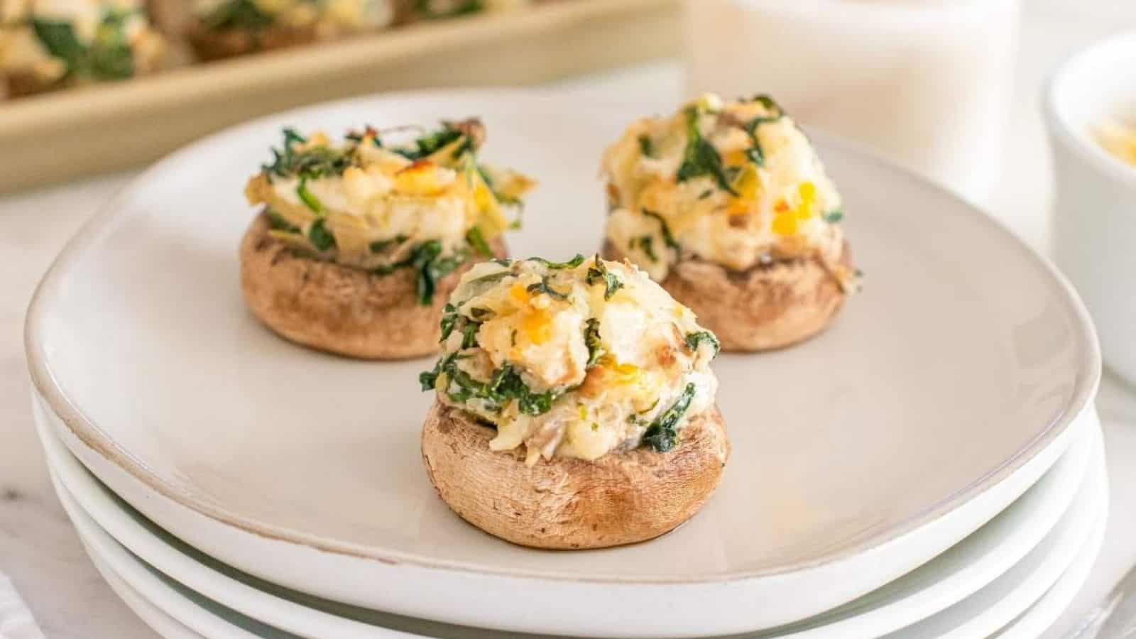 Three stuffed mushrooms on a white plate, topped with a mixture of cheese, herbs, and vegetables. .