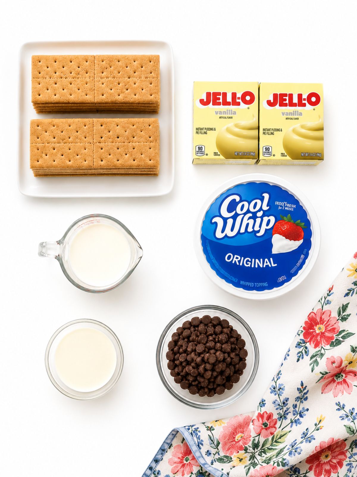 Chocolate eclair pudding pie ingredients arranged on a white background including graham crackers, vanilla pudding mix, Cool Whip, milk, heavy cream, and chocolate chips.