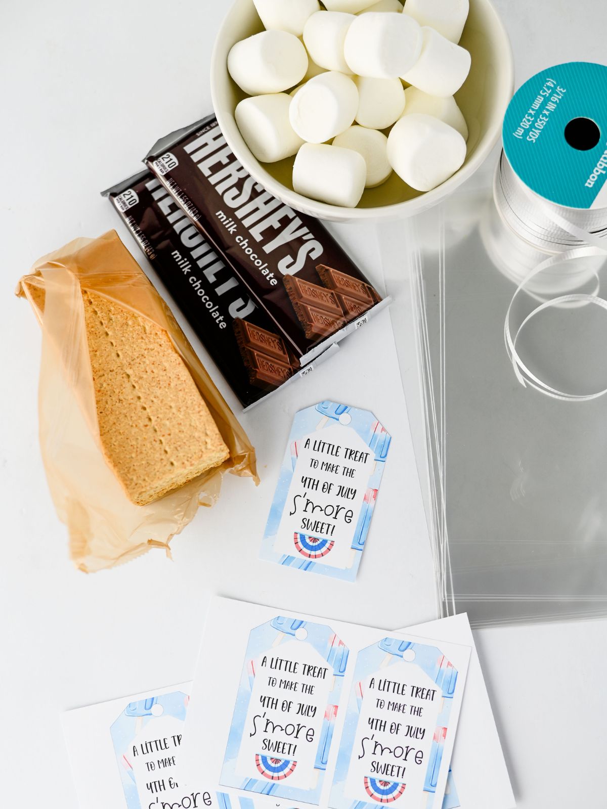 Ingredients for s’mores to go including graham crackers, Hershey’s chocolate bars, marshmallows, bags, and printable tags.