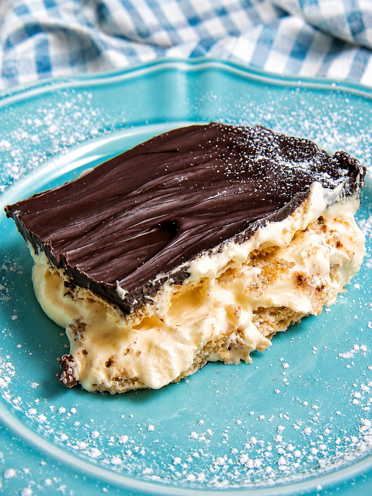 Chocolate eclair pudding pie slice with creamy filling and chocolate topping served on a turquoise dessert plate.