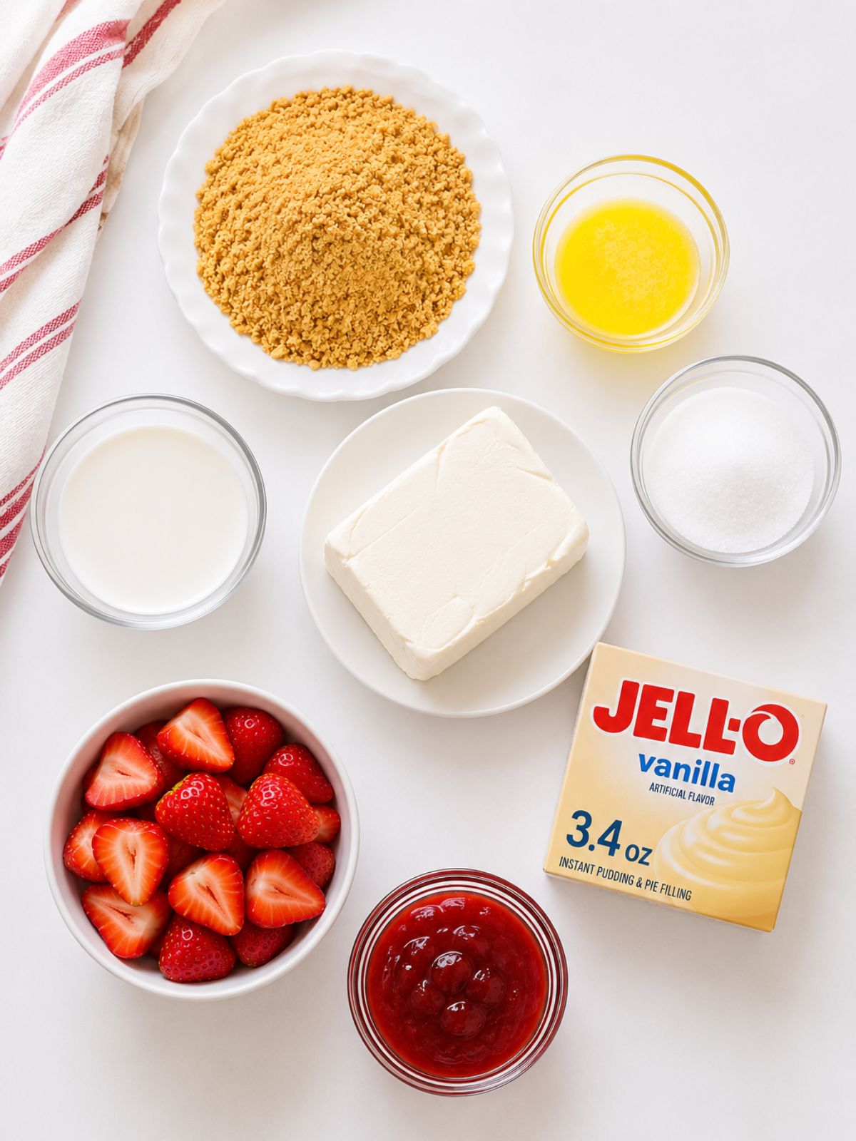 Ingredients for mini cream cheese vanilla pudding dessert including graham cracker crumbs, cream cheese, strawberries, strawberry jam, milk, sugar, butter, and vanilla pudding mix on a white background.