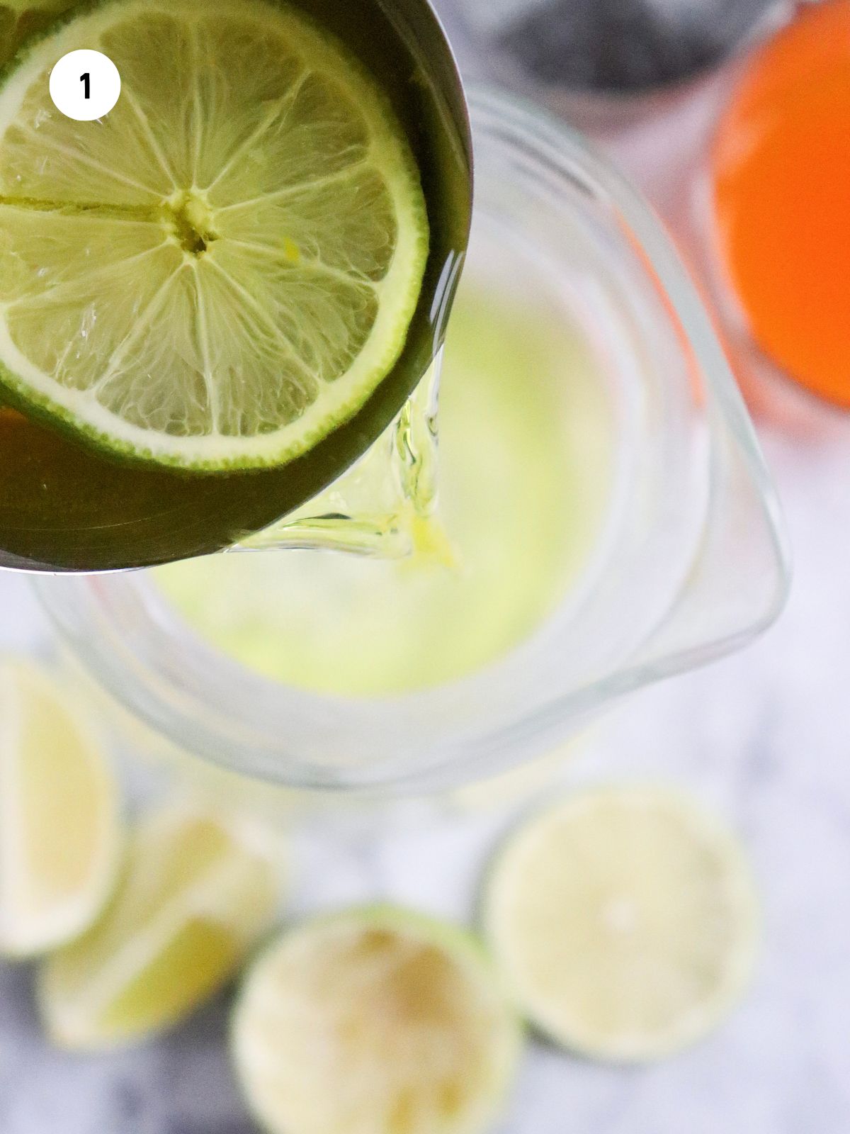 Fresh lime juice being poured into a pitcher for an orange juice mocktail recipe.