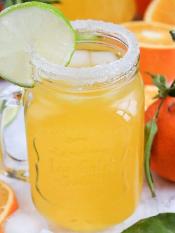 Refreshing orange juice mocktail served over ice with a lime garnish and salted rim.