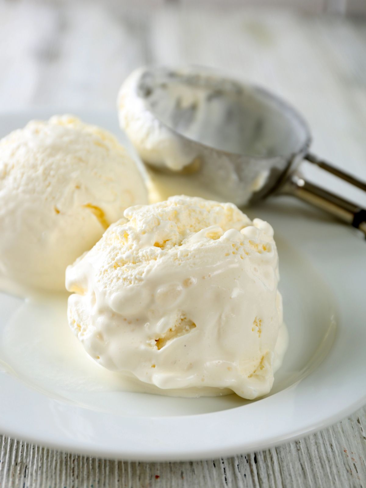soft scoops of homemade vanilla ice cream on a plate with ice cream scoop.