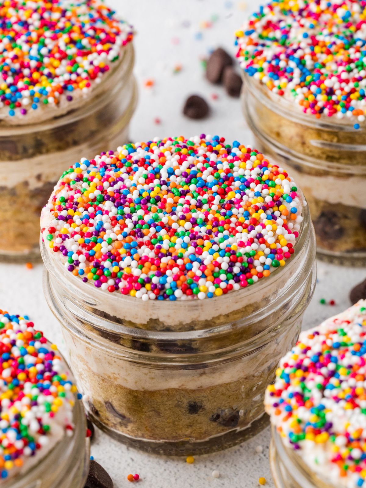 Chocolate chip cake layered with frosting in mason jars and topped with colorful rainbow sprinkles.