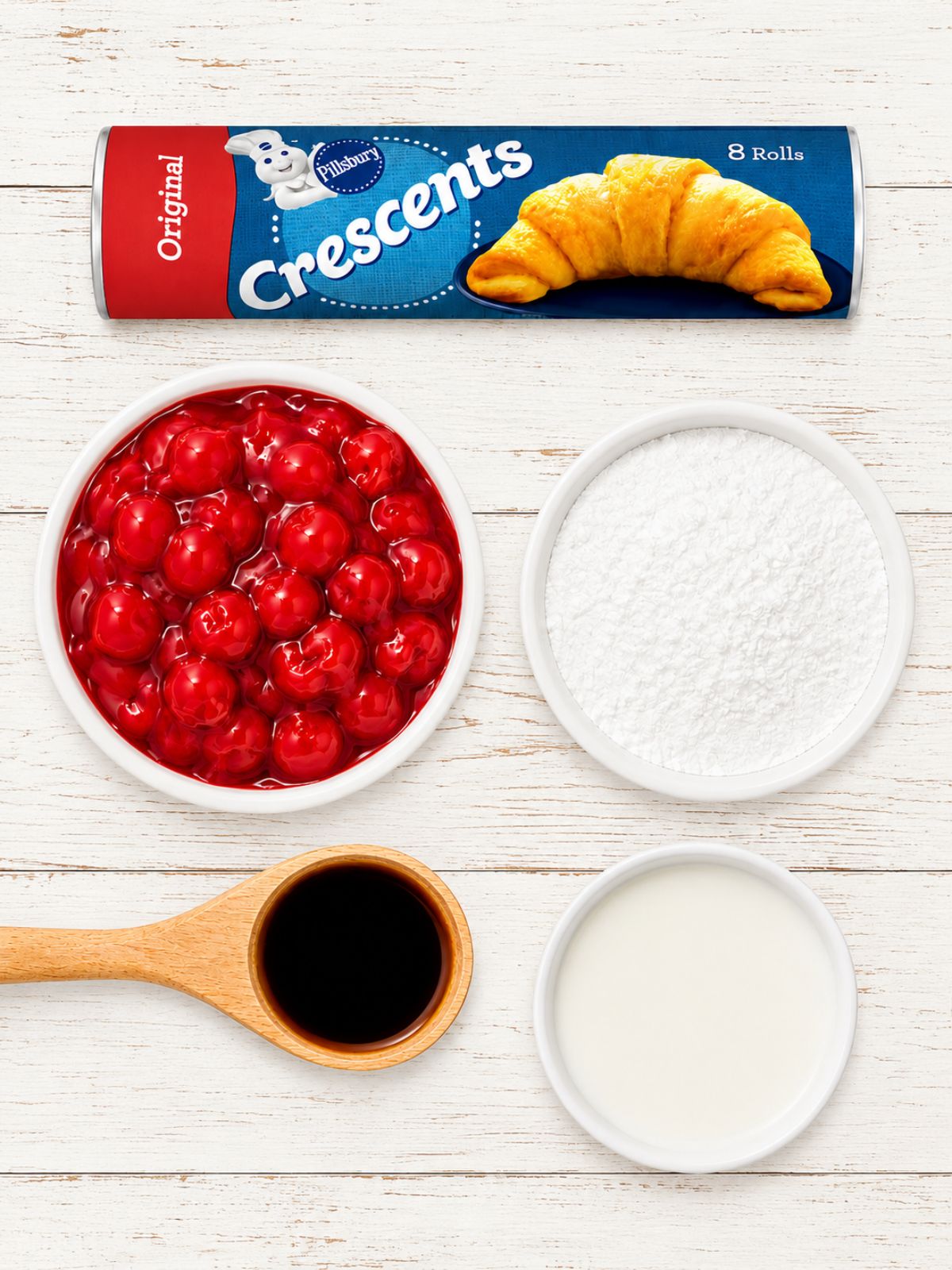 Overhead view of ingredients for cherry crescent rolls on a whitewashed rustic wood background, including Pillsbury crescent roll dough, cherry pie filling, powdered sugar, vanilla extract, and milk.