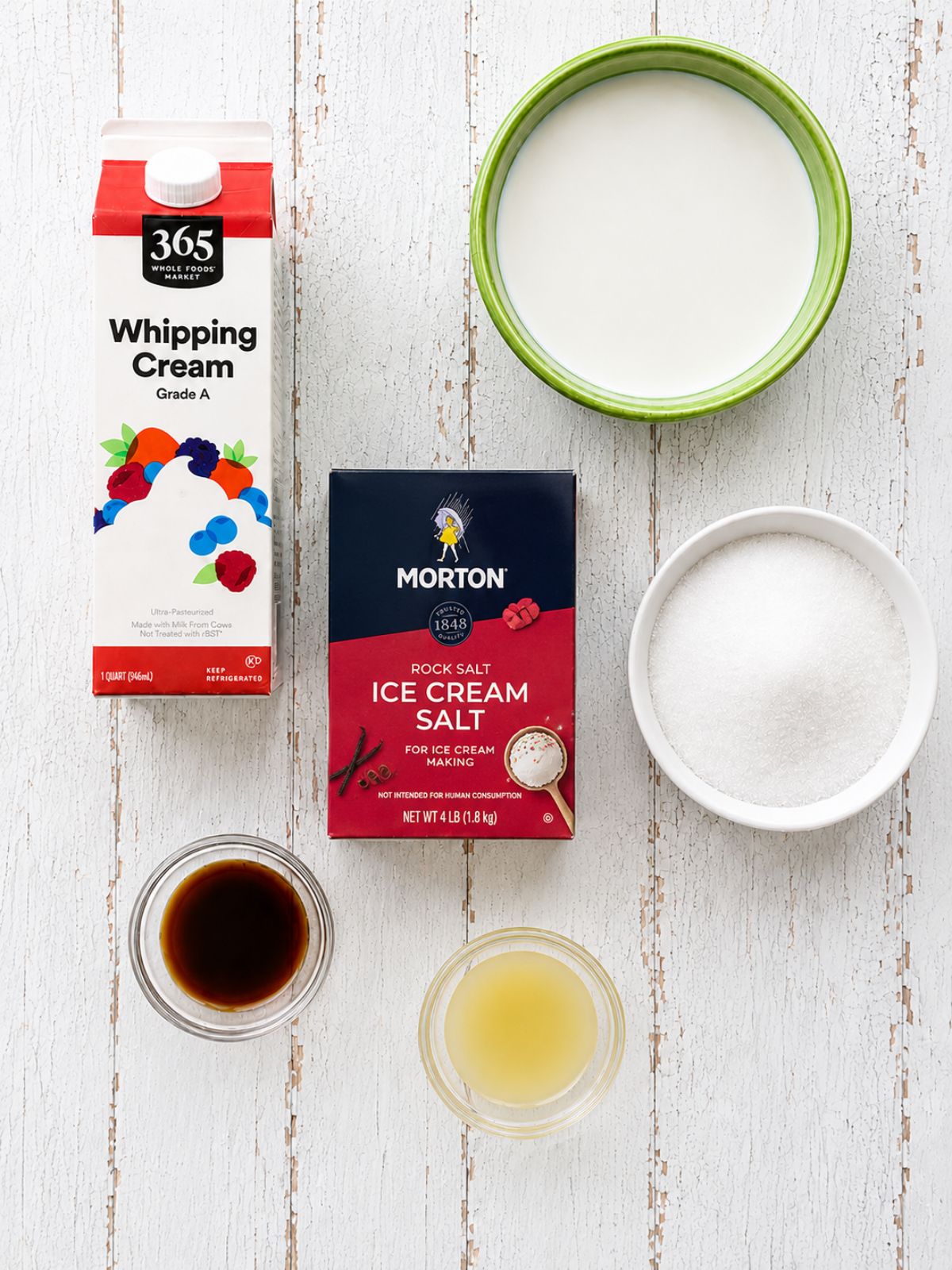 Ingredients for homemade vanilla ice cream including whipping cream, whole milk, sugar, vanilla extract, lemon juice, and ice cream salt.