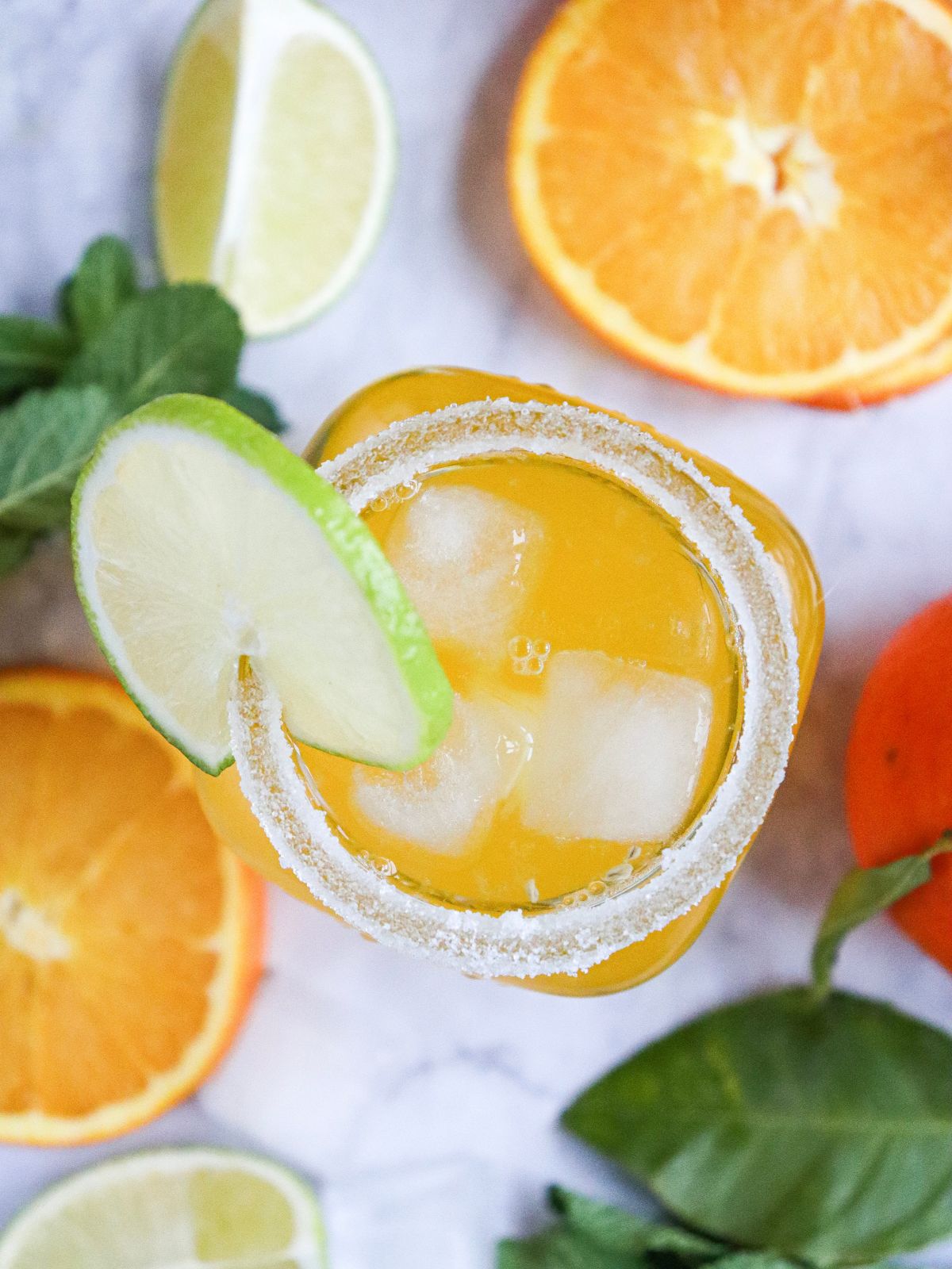 Orange juice mocktail with a salted rim, fresh lime garnish, and ice cubes served in a glass.
