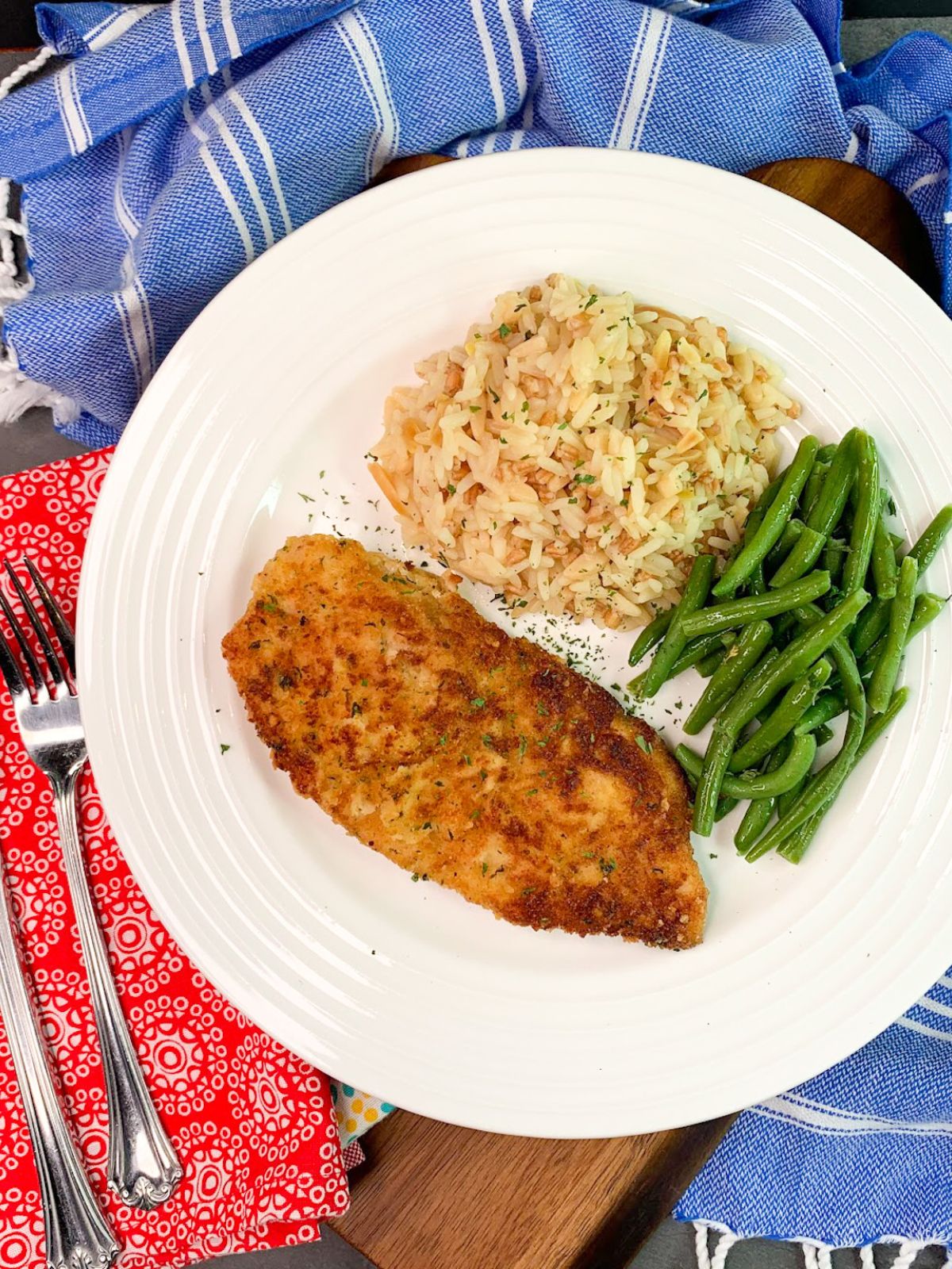 Breaded chicken cutlet served with rice pilaf and green beans on a white dinner plate.