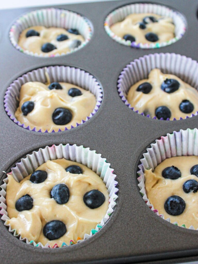muffin pan with unbaked muffin batter with blueberries on top.