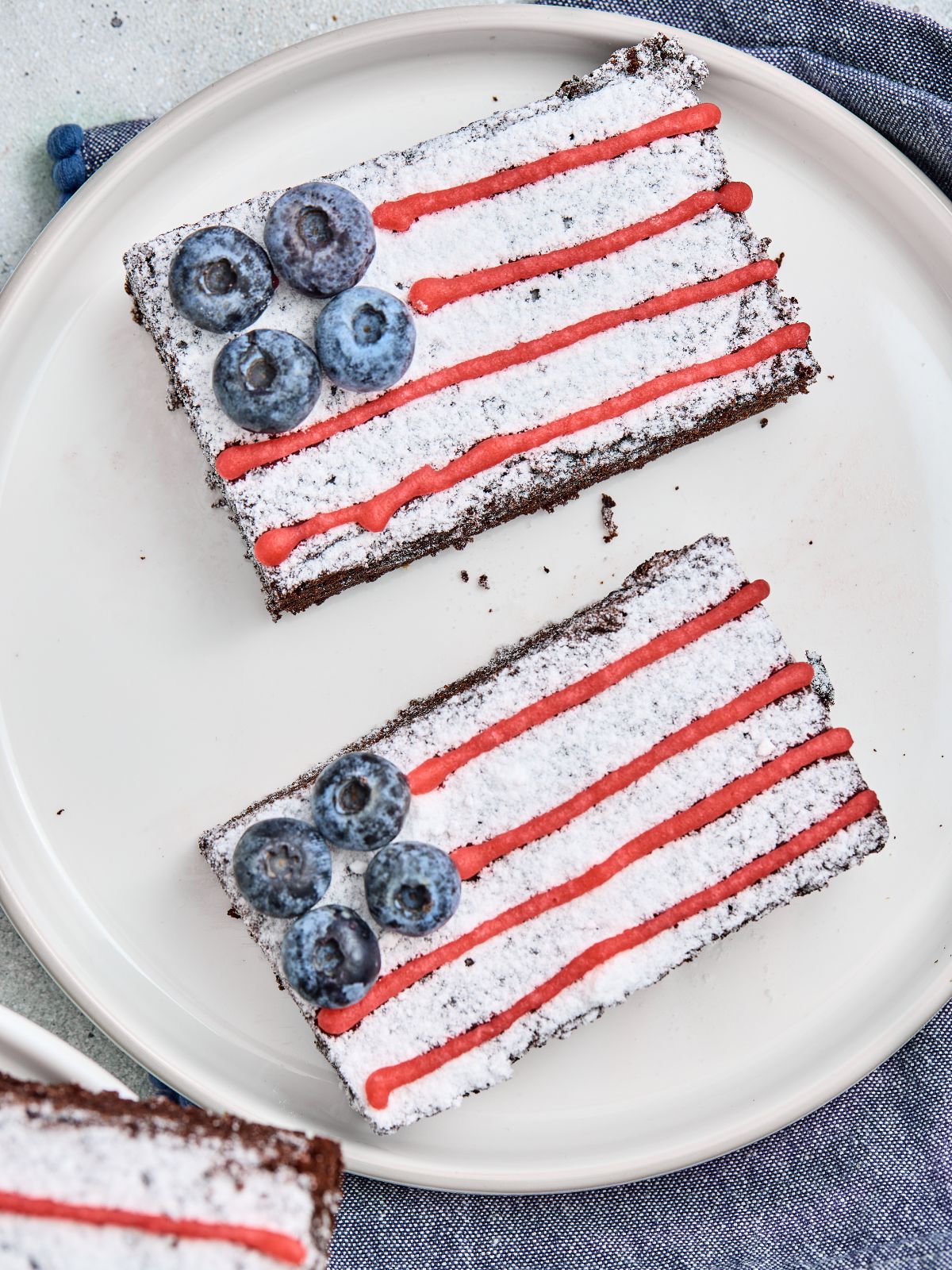 American Flag Brownies decorated with powdered sugar, red icing, and fresh blueberries served on a white plate.