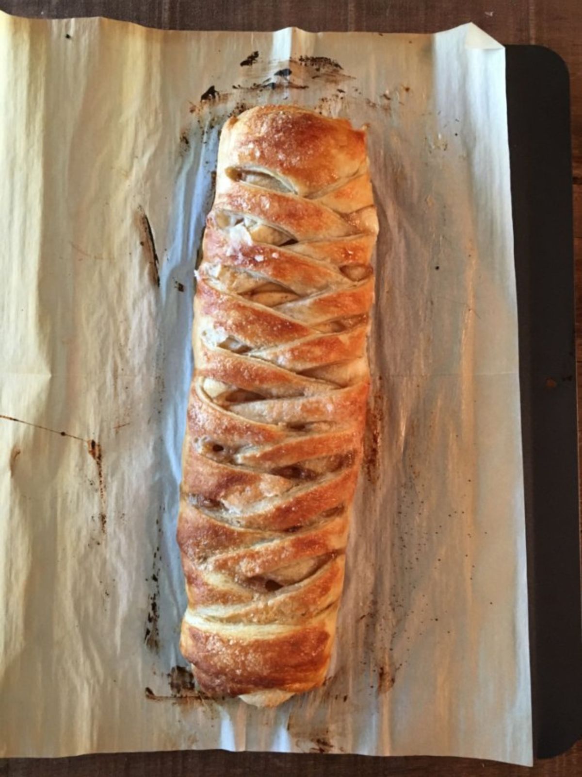 baked puff pastry braid with apples and cream cheese filling on baking tray and parchment paper.