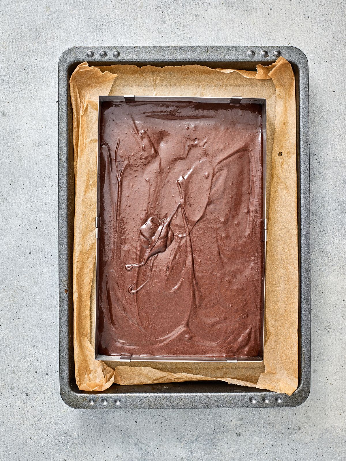 Brownie batter spread evenly in a parchment-lined baking pan before baking.