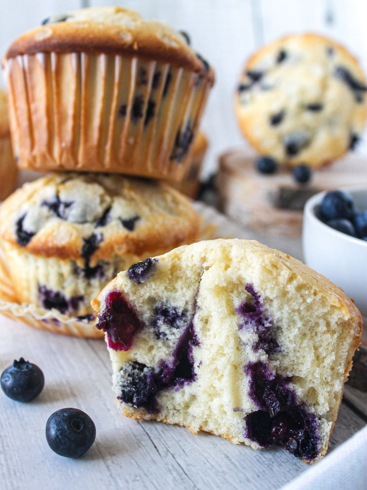 stacked classic blueberry muffins with one muffin in the front but open to show the inside of a baked muffin.