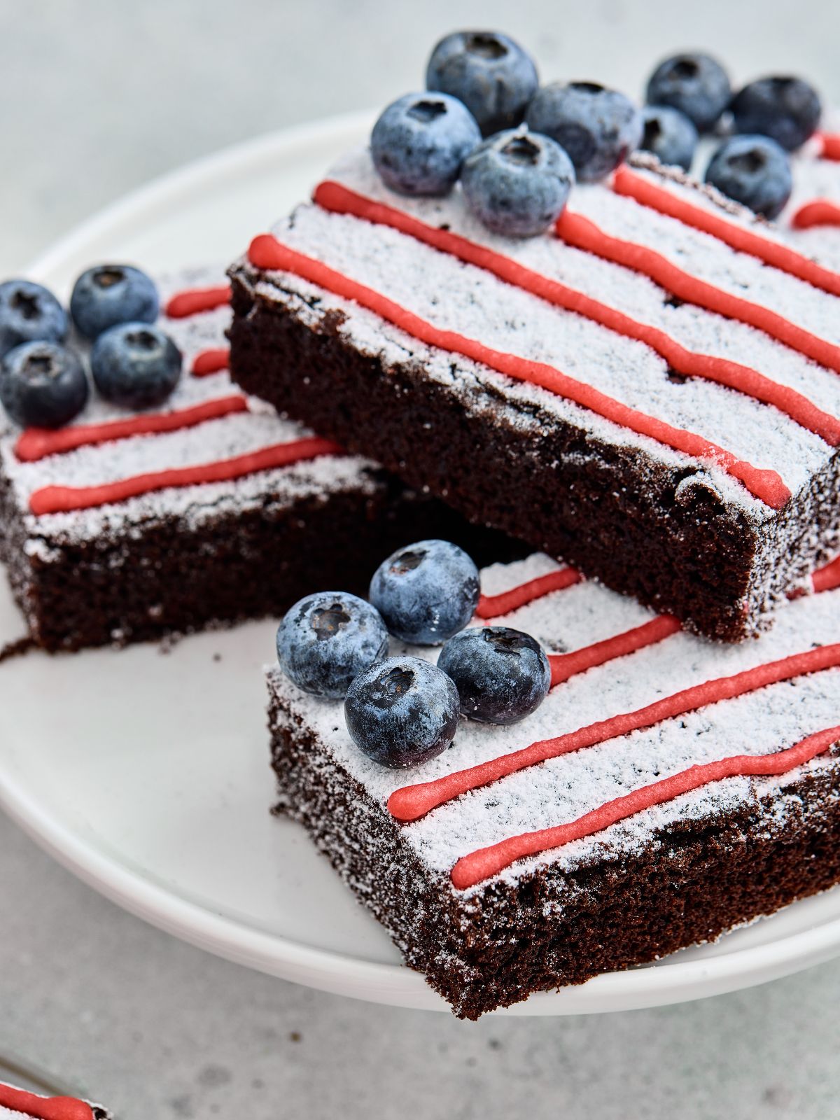 Stacked American Flag Brownies decorated with powdered sugar, red icing, and fresh blueberries.