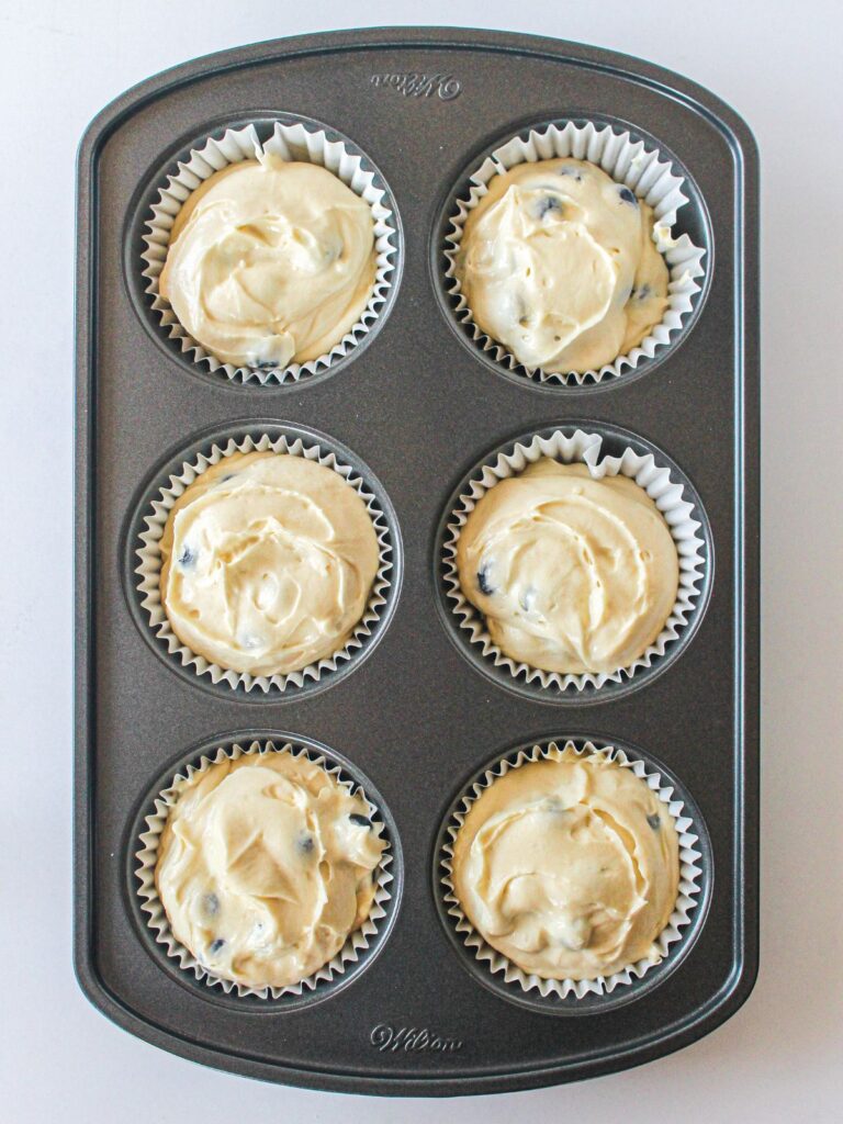 muffin batter in paper cups in muffin baking pan.