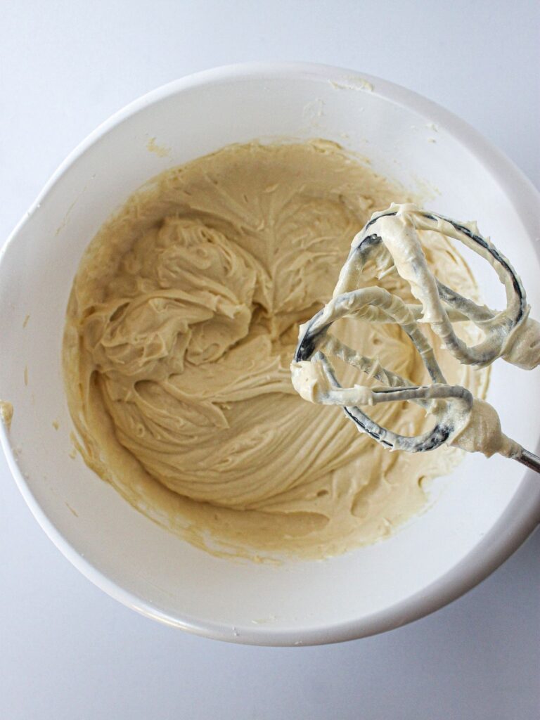 preparing muffin batter in white bowl with mixer beaters.