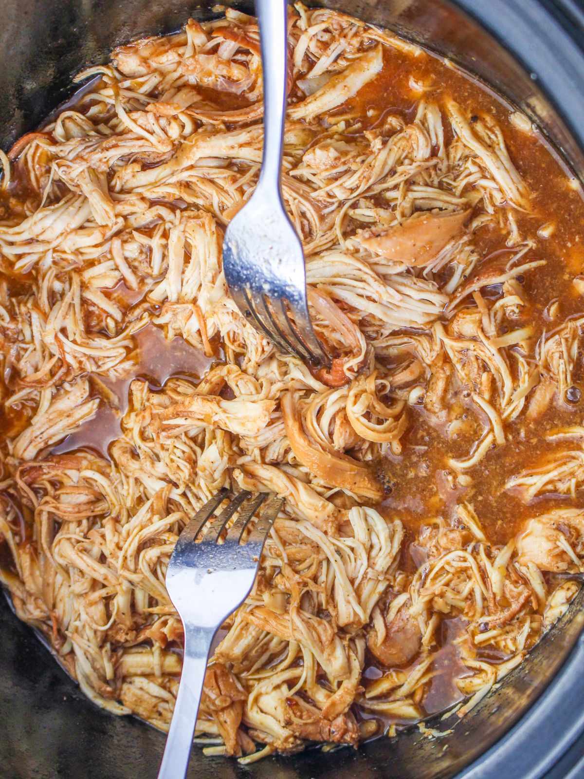 cooked shredded bbq chicken in crock pot with two forks.